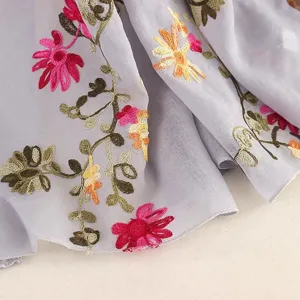 Close up view of lightweight sheer scarf detail with colorful floral embroidery texture.