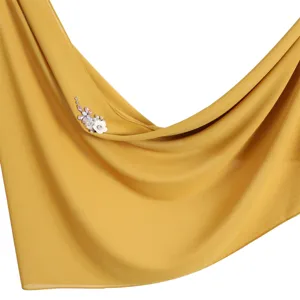 Detailed shot of yellow chiffon hijab scarf featuring sparkling rhinestone dragonfly and flower.
