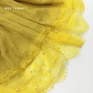 Detail van de gele kant sjaal met delicate bloemafwerking en parelversieringen op zachte stof.