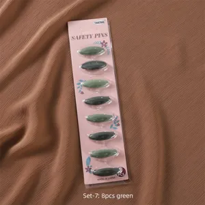 Detail view of green plastic safety hijab pins card pack, secure scarf clips for daily wear.