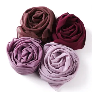 Detailansicht von vier weichen Chiffon-Tuschals, die in eleganten Lilatönen als Rosen gerollt sind.
