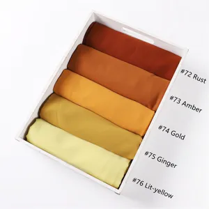 Detailansicht einfarbiger Chiffon-Kopftücher in warmen Farben ordentlich im Holztablett.