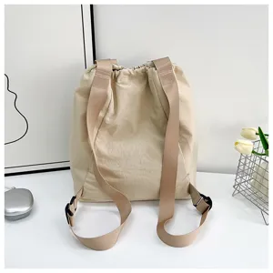 Beige drawstring bucket backpack detail showing wide straps and adjustable plastic buckles.