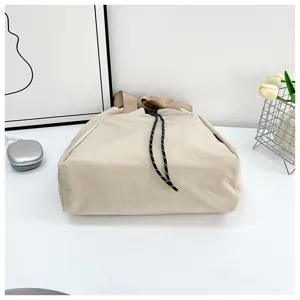 Detailed view of the casual beige drawstring bucket bag, highlighting the wide strap and cords.