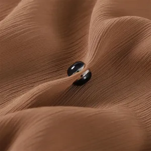 Nahaufnahme Detail der runden magnetischen Schal- und Tuchklemme an braunem Plissee.