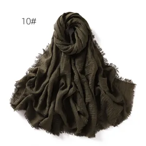 Close-up of dark green crinkled cotton linen scarf, frayed edges, breathable sun protection shawl.