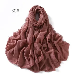 Close-up of a solid color crinkled linen gauze scarf with frayed tassel edges, soft drape.