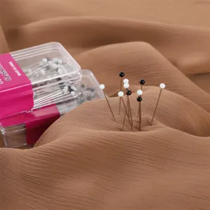 Primo piano di spilli con testa di vetro nera e bianca inseriti in un tessuto marrone.