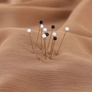 Dettaglio in primo piano di spille con testa di perla nera e bianca inserite in tessuto.
