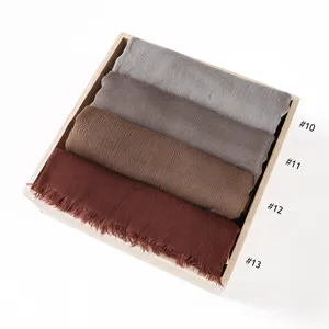 Detail shot of rolled solid color rayon soft wrinkled scarves with fringe in wooden tray.