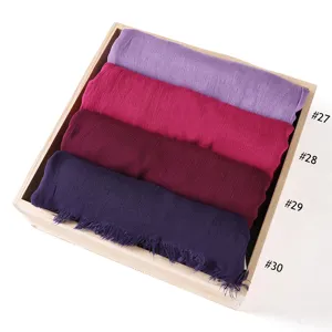 Close-up detail of rolled plain rayon wrinkle scarves with short fringes in wooden display.
