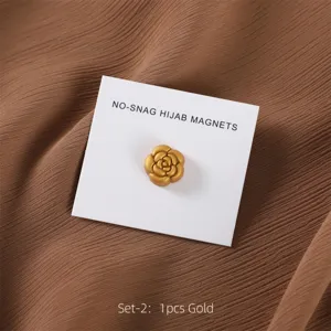 Gedetailleerd detail van een gouden camelia hijab magneet op witte kaart, bruine stof.