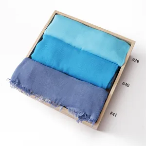 Detail shot of crumpled rayon solid color short tassel scarves in blue tones inside wooden tray.