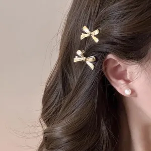Vue détaillée de petites pinces à cheveux nœud doré, accessoires élégants en métal pour femmes.