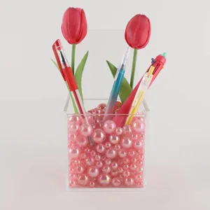 Transparent acrylic pen holder filled with pink shiny beads and decorative artificial tulips.