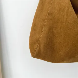 Close-up detail of brown faux suede shoulder bag showing fine stitching and soft texture.