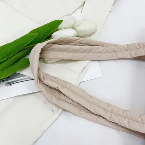 Close-up detail of soft quilted nylon tote bag strap with elegant white flower prop styling.