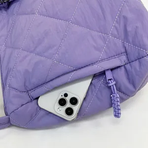 Close-up detail of purple quilted nylon puffer bag showing zippered pocket with phone inside.