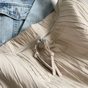 Primo piano dettagliato di una borsa a sacco beige plissettata con texture e doppie zip.