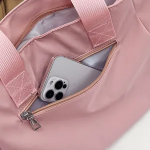 Pink nylon tote bag detail view showing front zipper pocket and sturdy shoulder straps.