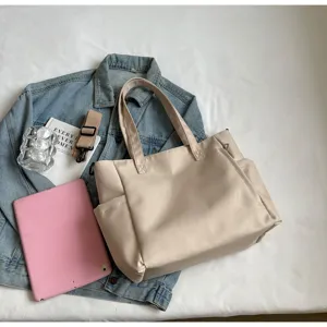 Detail shot of the beige nylon tote bag on a denim jacket background, showing side pockets.