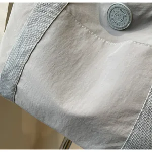 Detailopname van de lichte grijze nylon tas met fijne textuur, brede band en logopatch.