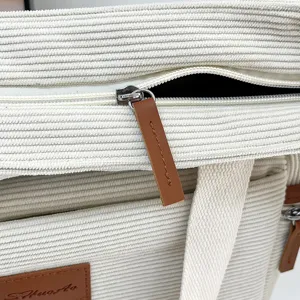 White corduroy tote bag detail shot, stylish canvas handbag with zipper and leather pull.