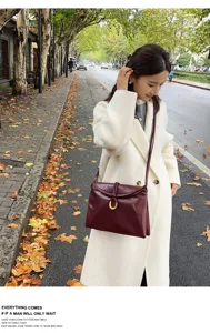 Detailed shot of dark red leather crossbody bag with metal horseshoe buckle on autumn street.