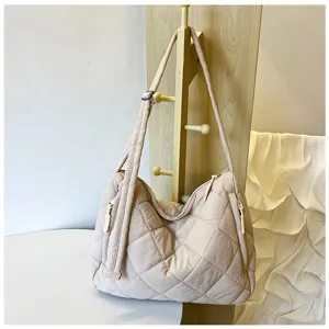 Close-up detail of the beige quilted nylon puffer shoulder tote bag hanging on wooden rack.