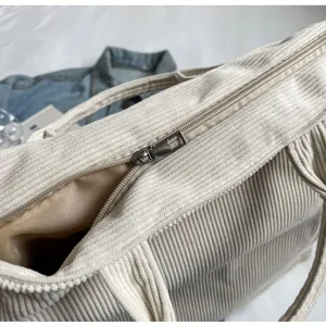 Close-up detail of beige corduroy tote bag showing zipper closure and soft texture.