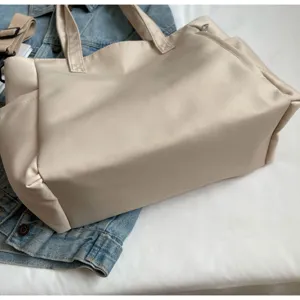 Detailed view of the beige nylon tote bag showing texture, large capacity, and side pockets.