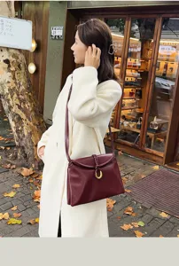 Outdoor lifestyle detail of dark red soft leather envelope shoulder bag with metallic ring clasp.