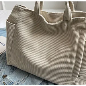 Close-up detail of casual beige corduroy tote bag, showing fine vertical texture and straps.