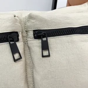 Close-up detail of casual nylon crossbody bag with multi zipper pockets and black square pull.