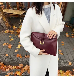 Detailed view of women burgundy soft leather clutch bag with braided knot and metal ring.