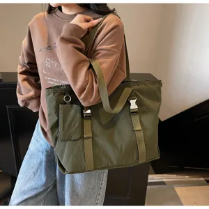 Detail view of large green canvas tote bag featuring buckle straps and side pouch.