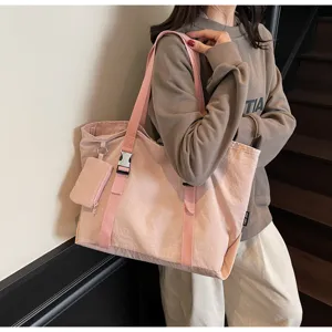 Close-up detail of a pink canvas tote bag with shoulder straps, buckles, and a mini pouch.