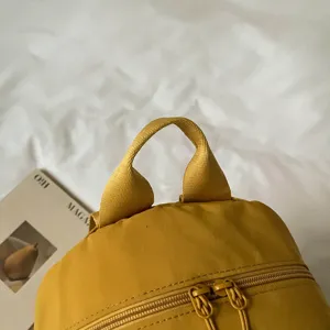 Close-up detail of yellow nylon backpack handle and zipper showing fabric texture and craftsmanship.