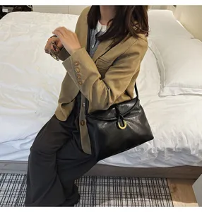 Close-up detail of black soft leather shoulder bag with gold horseshoe buckle and braided knot.