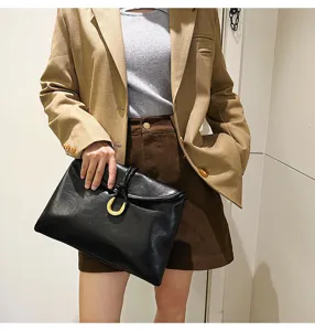 Detail shot of a black soft leather envelope bag featuring a gold horseshoe buckle and braided handle.