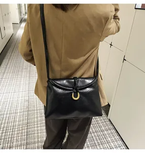 Minimalist black soft leather shoulder bag detail, horseshoe metal clasp, envelope style.