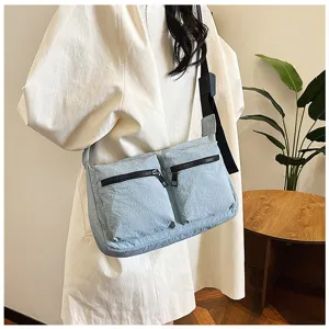 Detail shot of a light blue multi-pocket crossbody shoulder bag worn by a model in a clean room.