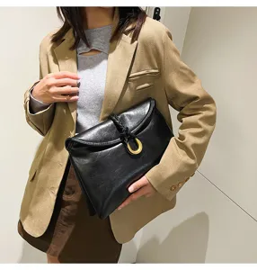 Black soft leather envelope clutch bag detail with metal horseshoe ring and braided knot.