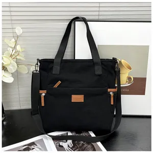 Black corduroy tote bag detail showing front zipper pocket, leather patch and sturdy handles.