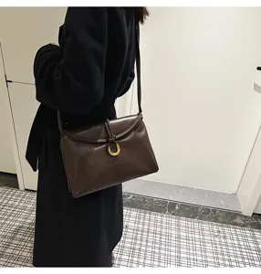Detail view of minimalist brown leather envelope shoulder bag with elegant metal buckle and strap.