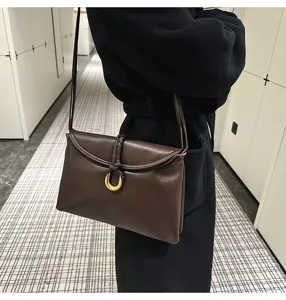 Detail view of the brown leather shoulder bag featuring a chic braided knot and gold ring clasps.