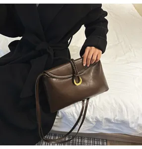 Close-up dark brown leather shoulder bag detail, soft envelope design with gold hardware ring.