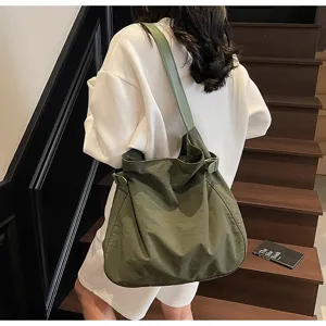 Detailed shot of the minimalist dark green nylon shoulder bag worn by model on stairs.
