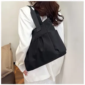 Black nylon tote bag detail view, casual shoulder bag with wide strap and front pockets.