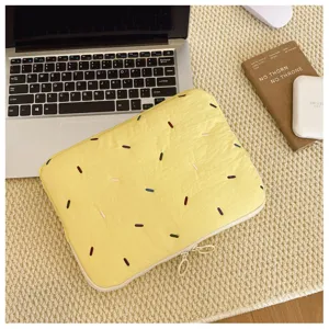 Detail shot of a pastel yellow quilted 14-inch laptop sleeve with colorful embroidery.